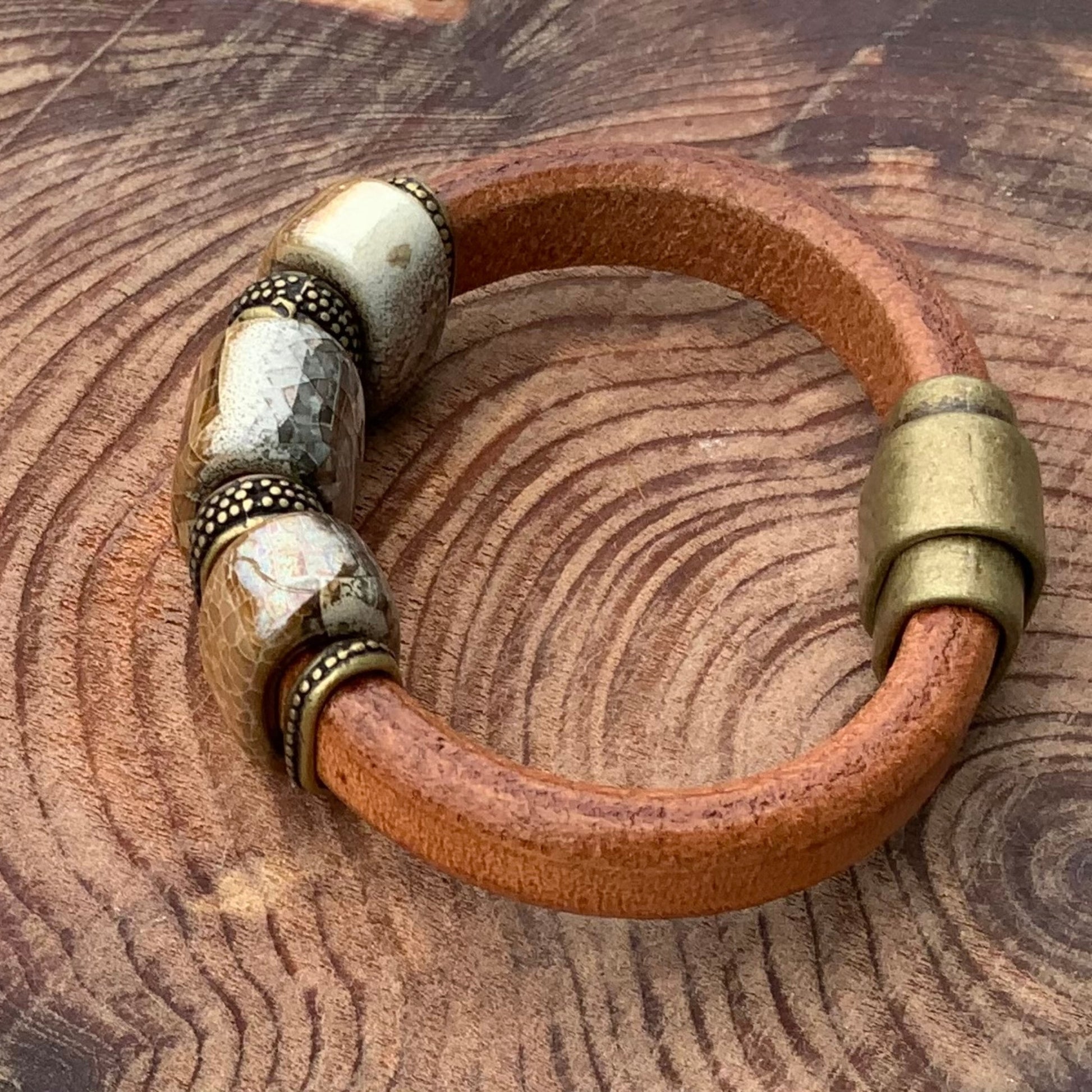 Genuine leather River Rock Ceramic Bracelet showcasing unique handmade ceramic beads in tan and gray with brass closure.